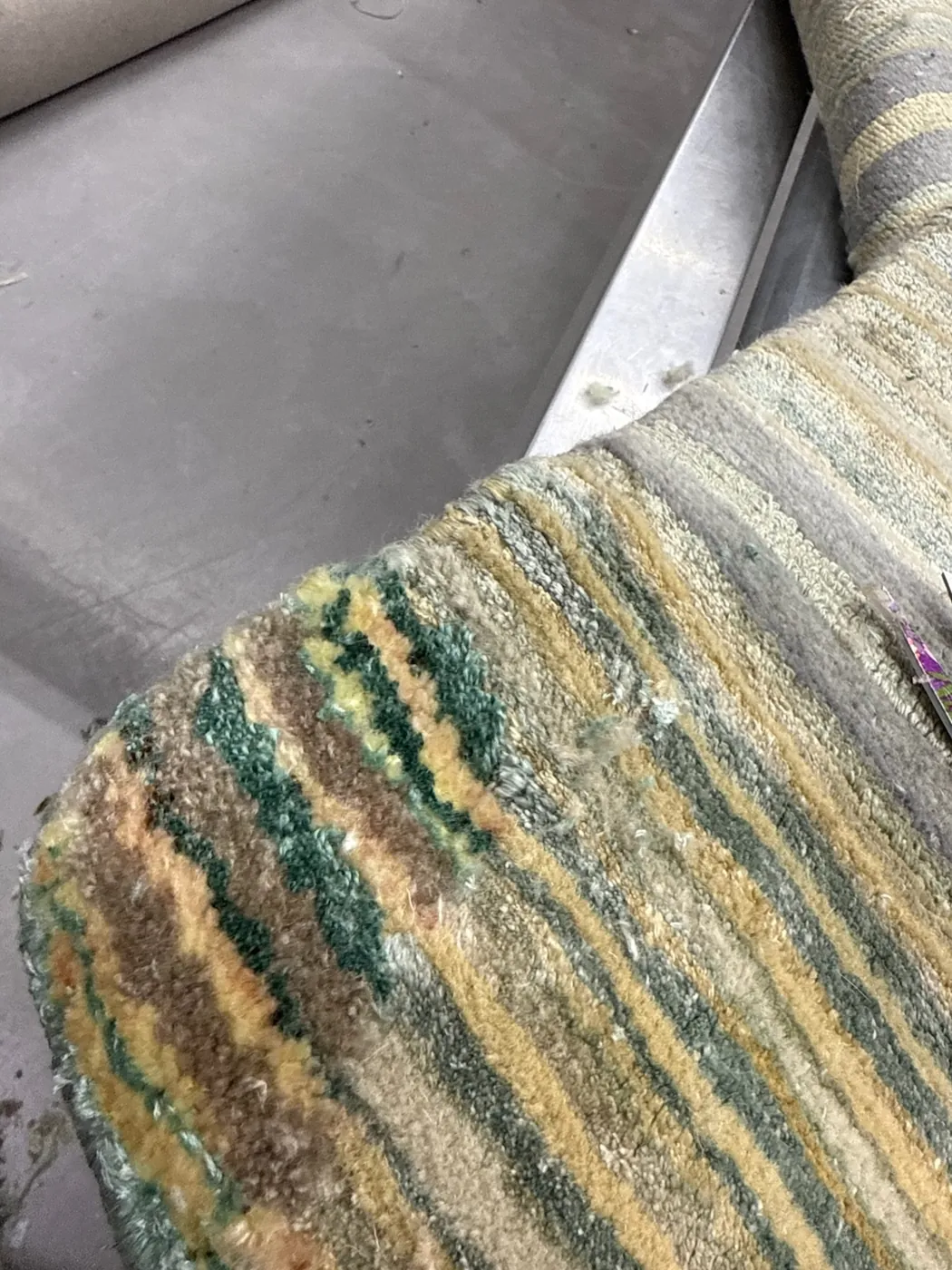 Green and cream rug with an area of pile loss and loose fibres