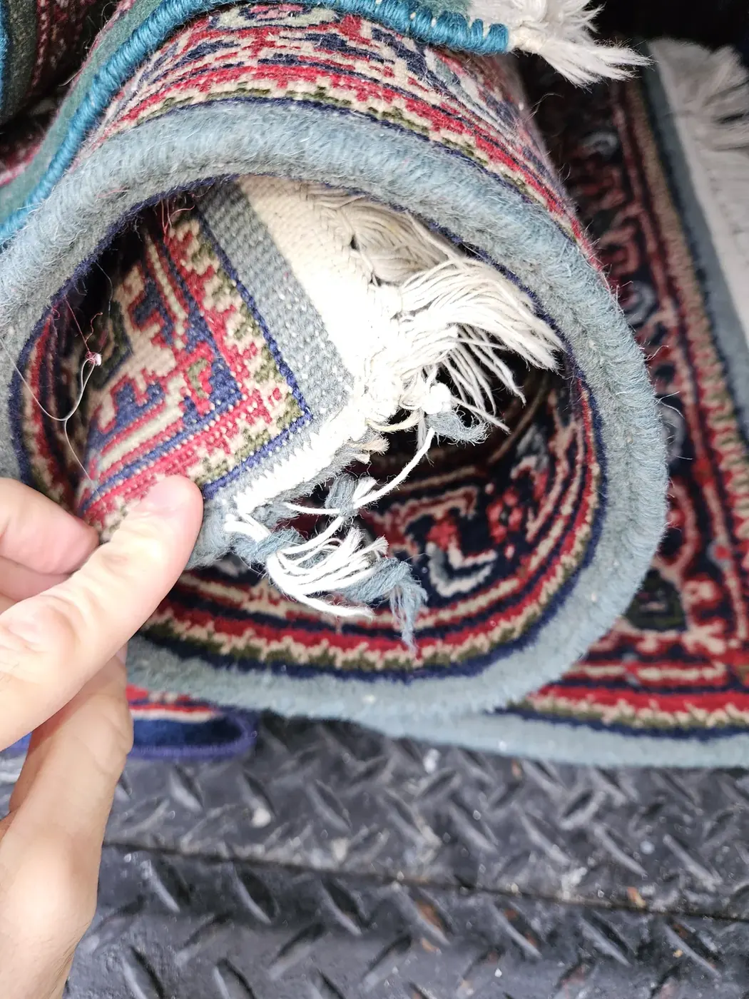 Hand at the damaged fringe of a rolled red rug